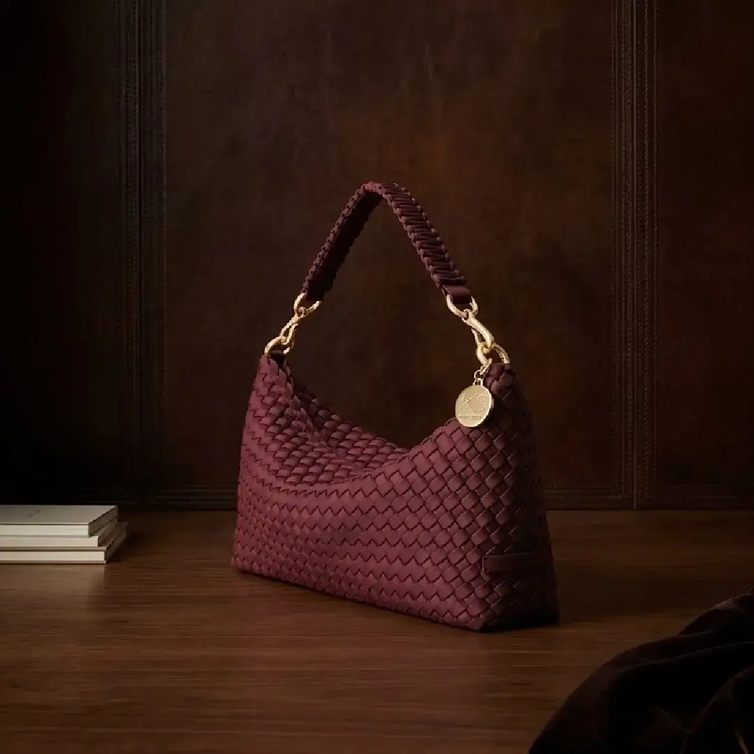 Premium dark burgundy hand-woven leather hobo shoulder bag with a braided strap and gold hardware set against a luxury dark wood background