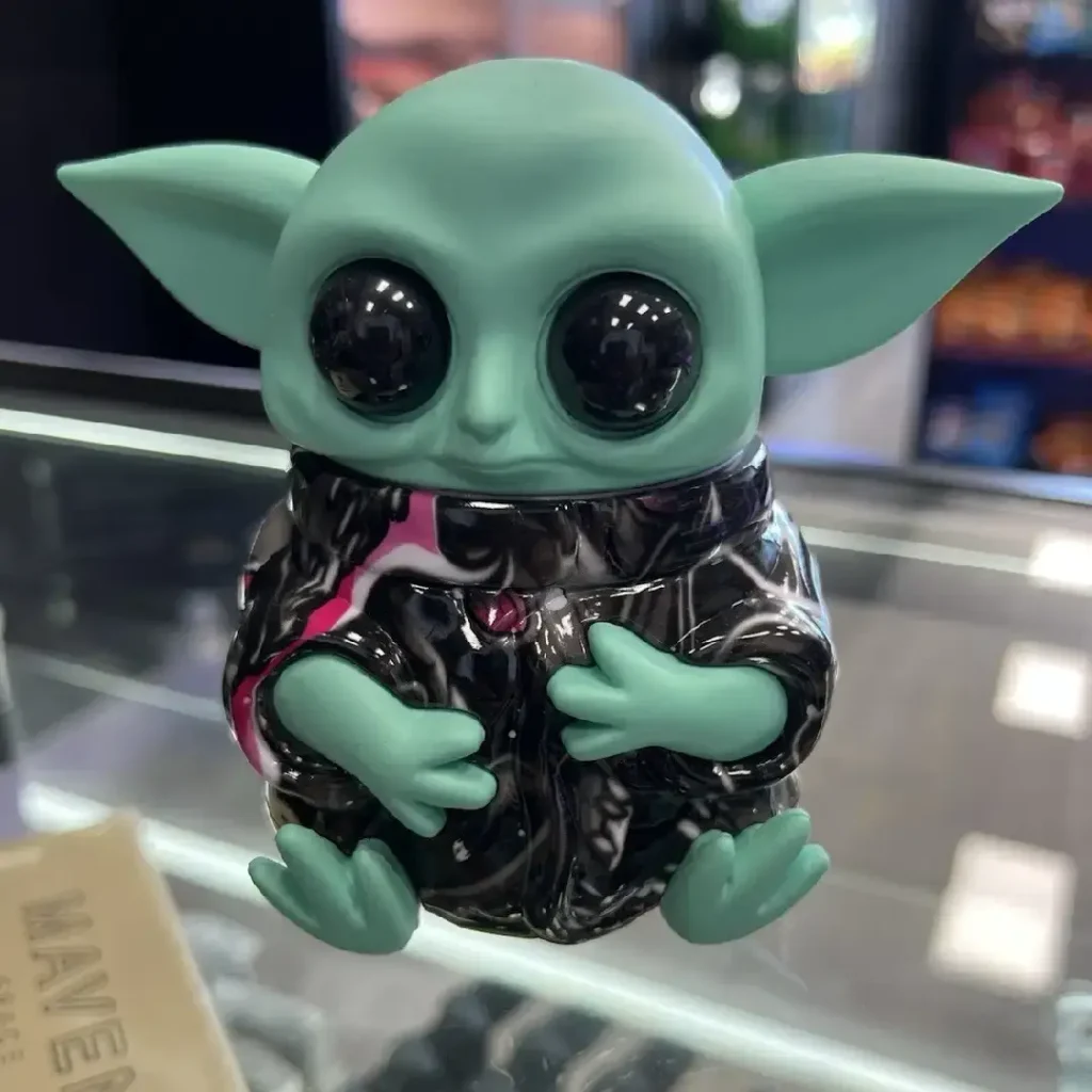 Front view of the Grogu Baby Yoda grinder sitting on a glass display counter.